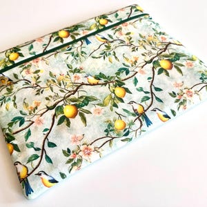 Può includere: Una pochette rettangolare in tessuto con cerniera su sfondo azzurro, caratterizzata da un motivo ripetuto di limoni gialli, foglie verdi, rami marroni, fiori rosa e piccoli uccelli con piume blu e gialle, rifinita con una zip verde scuro.