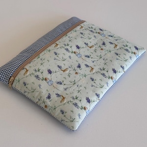 Könnte beinhalten: Ein rechteckiger, gesteppter Beutel mit einem hellblauen Blumenmuster mit Vögeln und Lavendel. Der obere Rand ist ein blau-weißes Vichy-Muster mit einem beigefarbenen Reißverschluss. Der Beutel ist etwa 30 cm breit und 23 cm hoch.