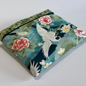 Può includere: Pochette quadrata in tessuto con un design di ispirazione giapponese. La pochette presenta una gru, fiori rosa e gialli e uno sfondo verde acqua con motivi a onde. Il bordo superiore è verde con un bordo nero.