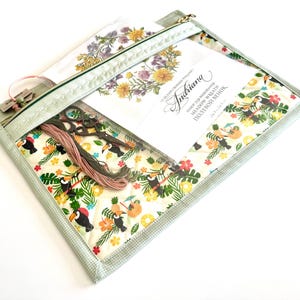Puede incluir: Una bolsa transparente con cremallera y borde de cuadros verdes, que contiene suministros de bordado. En el interior hay tijeras, hilo y un diseño impreso con motivos florales y tucanes. La bolsa tiene un diseño floral en la parte posterior y una etiqueta con texto.