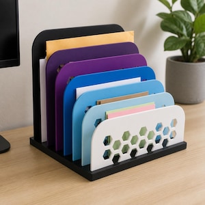 Pode incluir: Um organizador de documentos de mesa em camadas com uma base preta e seis divisórias verticais em um gradiente de cores incluindo preto, roxo escuro, roxo claro, azul escuro, azul claro e branco, cada uma com um padrão hexagonal.