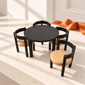 May include: A miniature dining set featuring a circular black table and three matching chairs with black frames and tan circular seats. The furniture pieces are arranged together, showcasing a consistent black wood-grain finish and neutral-toned cushions.