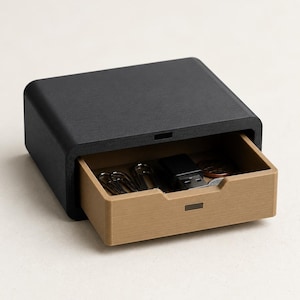 May include: A small, rectangular desk organizer featuring a matte black outer shell and a tan pull-out drawer. The open drawer contains several silver metal paper clips, a black USB flash drive, and a few small copper-colored coins.
