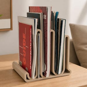 May include: A beige, U-shaped magazine rack made of a smooth, solid material. The rack features multiple vertical slots holding various magazines and booklets, including one with a prominent red cover featuring the word GUIDE in white text.