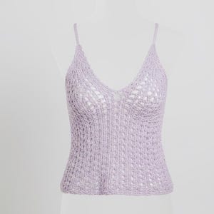 May include: A light purple crochet top with a V-neck and thin straps. The top is displayed on a white mannequin. The crochet pattern is open and airy, with a mix of solid and openwork sections. The overall style is delicate and summery.