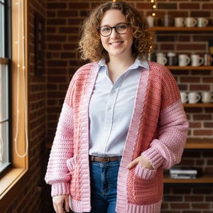 Puede incluir: Cárdigan de crochet hecho a mano, rosa y melocotón, con frente abierto. El suéter presenta un patrón de puntadas texturizadas, mangas largas y dos bolsillos delanteros. Se usa sobre una camisa azul claro y vaqueros azules.