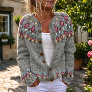 Peut inclure: Un gilet en tricot gris avec une encolure ronde et une fermeture boutonnée sur le devant. Le vêtement est orné d'un motif géométrique coloré dans des tons de rose, jaune et bleu clair sur les épaules et les poignets. Il est porté sur un haut blanc.
