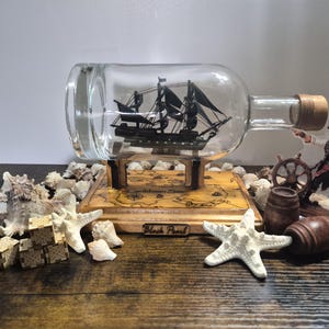 Handmade Black Pearl ship in a bottle with a wooden base and detailed features.