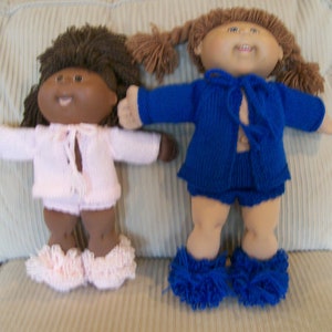 以下が含まれることがあります： ニットの服を着たキャベッジパッチキッズのドール2体。1体は茶色の髪にピンクのセーターとパンツ。もう1体は金髪に青いセーターとショートパンツを着ている。