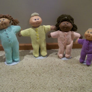 May include: Four Cabbage Patch Kids dolls wearing knitted pyjamas in different colours: light blue, yellow, pink and purple.