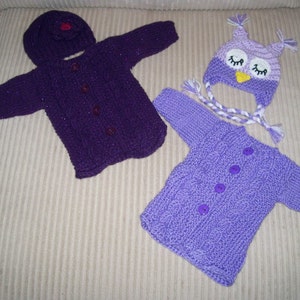 May include: A collection of hand-knitted baby clothes in purple hues. The set features a hooded cardigan with buttons, a matching hat, and an owl-shaped hat. The cardigans have a cable knit pattern. The owl hat has white and purple braided ties.