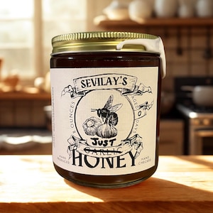 May include: A jar of Sevila's Just Garlic Honey, with a gold lid and a white label featuring a bee and garlic illustration. The jar contains a dark liquid and is labeled as 8 ounces.