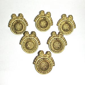 May include: A set of six circular brass drawer pulls, each featuring a central floral medallion, a swinging ring handle, and a decorative bow motif at the top. The metal hardware has a muted, aged gold finish with intricate relief detailing.