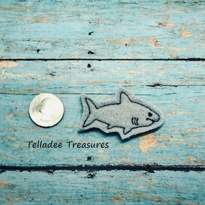 May include: A gray felt shark applique with black stitching. The shark is about the size of a US quarter.