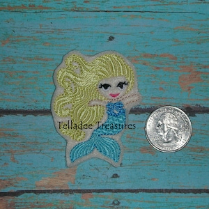 May include: Embroidered patch of a mermaid with long blonde hair, wearing a blue tail and holding a seashell. The patch is about the size of a quarter.