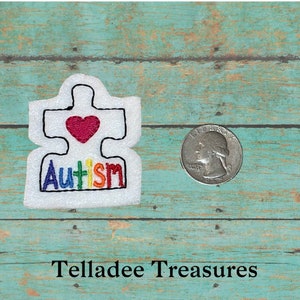 May include: White felt puzzle piece with a red heart and the word "Autism" in rainbow colors. The word "Autism" is embroidered in a rainbow pattern. The puzzle piece is about the size of a US quarter.