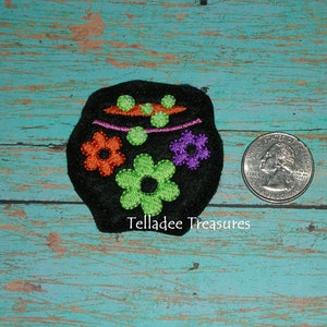 May include: Black felt skull with green, orange, and purple embroidered flowers. The skull is about the size of a US quarter.