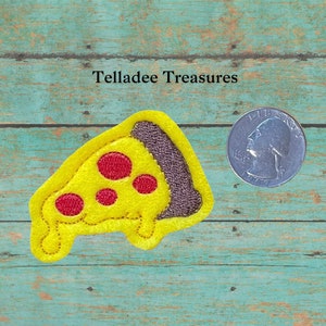 May include: A yellow felt pizza slice with red pepperoni and a brown crust. The pizza slice is about the size of a US quarter.