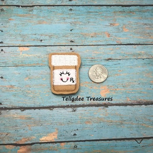 May include: A brown felt pill bottle with a smiling face and the letter "R" on the label. The bottle is about the size of a US quarter.