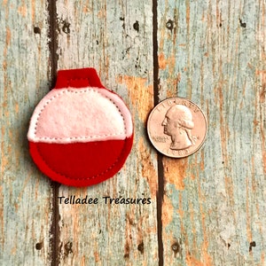May include: A red and white felt bobber ornament with a white felt top and a red felt bottom. The ornament is about the size of a US quarter.