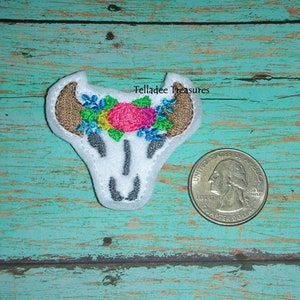 May include: White embroidered skull with a floral crown of pink, yellow, blue, and green flowers. The skull is about the size of a US quarter.