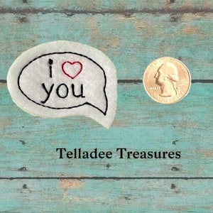 May include: White felt speech bubble with black embroidery that reads "I love you" with a red heart. The speech bubble is about the size of a US quarter.
