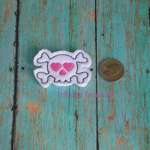 May include: White felt skull with pink hearts for eyes. The skull is about the size of a US quarter.