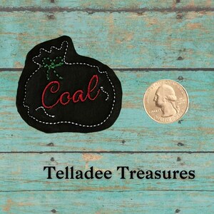 May include: A black felt Christmas stocking with white stitching and a green bow. The stocking is embroidered with the word "Coal" in red thread. The stocking is about the size of a US quarter.