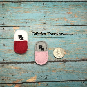 May include: Two felt pill shapes with an embroidered "Rx" on them. The pills are about the size of a US quarter.