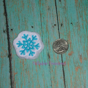 May include: A white felt snowflake applique with a turquoise blue embroidered snowflake design. The snowflake is about the size of a US quarter.