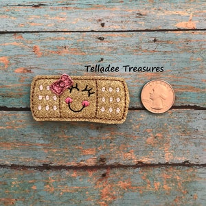 May include: A gold glitter bandage with a pink bow and a smiling face. The bandage is about the size of a US quarter.