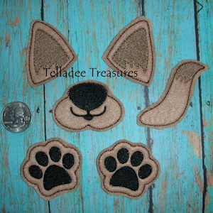 May include: A collection of brown and black felt dog-themed appliques, including ears, a nose, a tail, and paw prints. The text "Telladee Treasures" is visible. The appliques are displayed on a turquoise wooden surface.