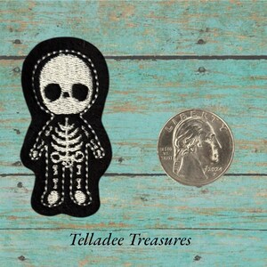 May include: A black and white embroidered skeleton patch. The patch features a cartoon skeleton design with a white embroidered skull and rib cage. The patch is next to a U.S. quarter coin for size reference.