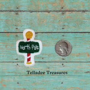 May include: A green and white felt patch with a candy cane pole and a sign that reads "North Pole". The patch is about the size of a US quarter.