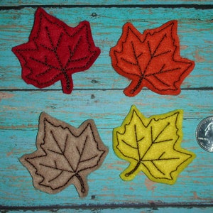 May include: Four felt maple leaves in different colors: red, orange, brown, and yellow. The leaves are approximately the size of a US quarter.