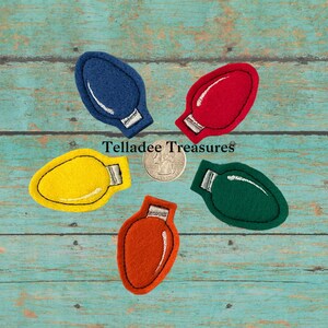 May include: Five felt Christmas light ornaments in different colors: blue, red, yellow, green, and orange. The ornaments are arranged in a circle on a blue wooden background. "Telladee Treasures" is written in white text on the background.
