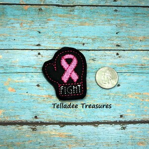 May include: Black felt boxing glove with a pink ribbon and the word "FIGHT" embroidered on it.