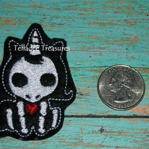 May include: A black and white embroidered patch of a skeleton unicorn with a red heart. The patch is about the size of a US quarter.