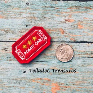 May include: Red felt ticket with white stitching and gold stars. The ticket says "Admit One".
