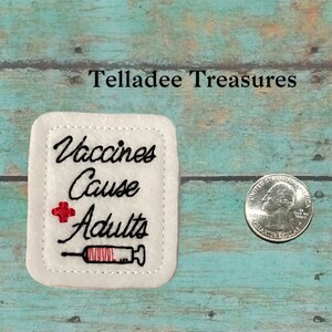 May include: White felt square patch with black embroidery that reads "Vaccines Cause Adults" with a red plus sign and a red and black embroidered syringe.