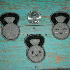 May include: Three gray felt kettlebell patches with black outlines. Two of the kettlebells have a smiling face with pink cheeks.