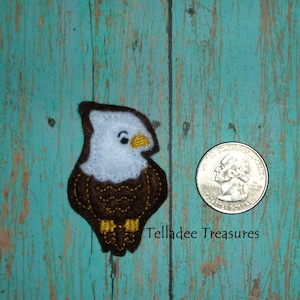 May include: A brown and white felt applique of a bald eagle with a yellow beak and feet. The eagle is about the size of a US quarter.