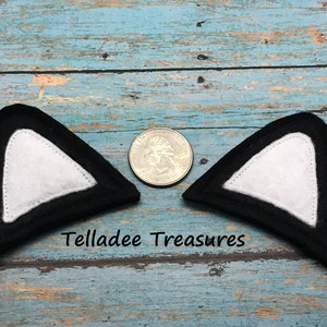 May include: Two black felt cat ears with white felt inside. The ears are about the size of a US quarter.