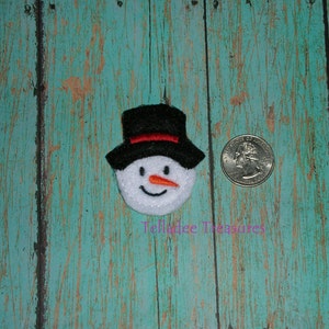 May include: A white felt snowman face with a black top hat, orange nose, and black eyes. The snowman face is about the size of a US quarter.