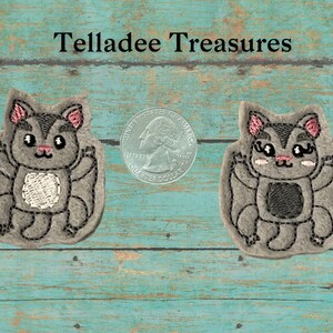May include: Two gray felt appliques of a cartoon flying squirrel with pink ears and black eyes. The appliques are about the size of a US quarter.