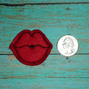 May include: A red felt applique of a pair of lips with a black outline. The applique is about the size of a US quarter.
