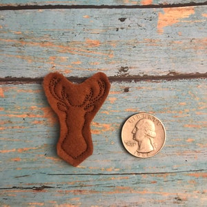 May include: A brown felt deer head applique with stitched details. The applique is about the size of a quarter.