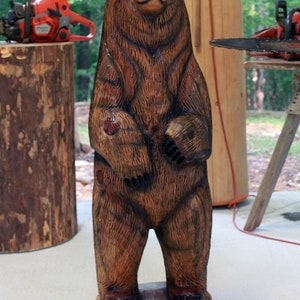 May include: A brown wooden bear sculpture carved in a standing position with its paws raised. The bear is standing on a wooden base.