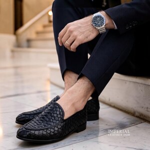 May include: Black woven leather loafers. The shoes have a textured basketweave design. The image also shows a silver wristwatch with a black face and a silver band. The shoes are part of a formal outfit.