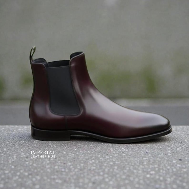 Pu&ograve; includere: Stivaletto Chelsea in pelle bordeaux lucida. Presenta un pannello laterale elastico nero e un tirante posteriore. La suola &egrave; nera. Il testo "IMPERIAL LEATHER HUB" &egrave; visibile. Un classico stivaletto.